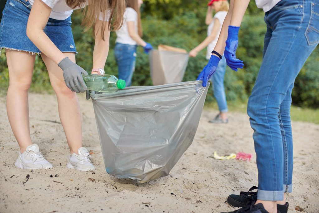 Group of teenagers on riverbank picking up plastic trash in bags